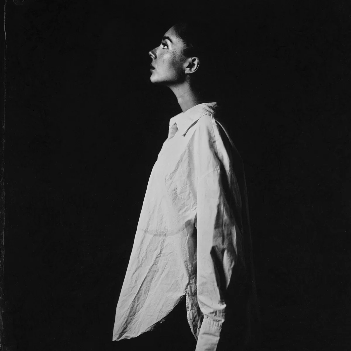 Девушка в профиль в белой рубашке на чёрном фоне, голова поднята